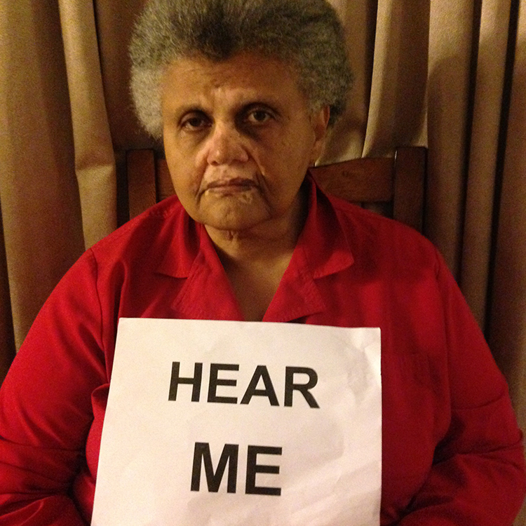 Picture of a woman in a red shirt holding a sign that says "Hear ME."