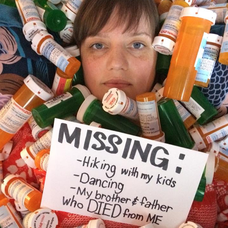 A woman buried among dozens of prescription pill bottles, with only her face visible There's a sign that reads, "Missing: Hiking with my kids, Dancing, My brother and father who DIED from ME."
